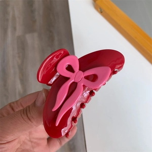 Détail de la pince à cheveux en acétate rouge avec un nœud rose 3D pour le style