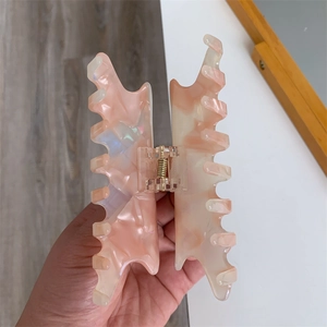 Macro shot of large pink acetate hair claw clip with golden metal spring and marble texture