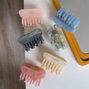 Close-up of rectangular acetate hair claws in various marble colors with gold metal logo