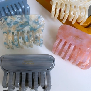 Macro detail of acetate hair claw clips with elegant golden logo on marble finish