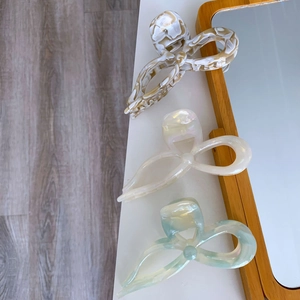 Close-up of three acetate bow hair claws in amber marble, pearl white, and light blue finishes
