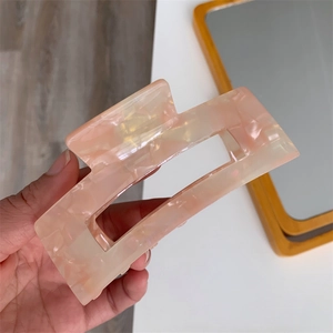 Detail view of large pink marble acetate hair claw clip held by hand for thick hair styling