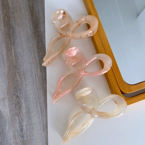 Three acetate bow claw clips in amber, pink, and cream pearl on a minimalist desk
