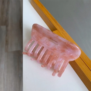 Detail of pink marble acetate hair claw with golden lettering and accordion style teeth