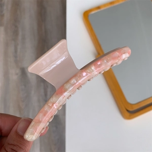 Detail shot of the pink marble textured acetate hair claw clip held by hand