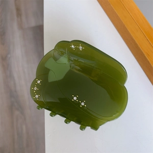 Détail de la pince à cheveux en forme de poivron vert avec strass sur surface en acétate
