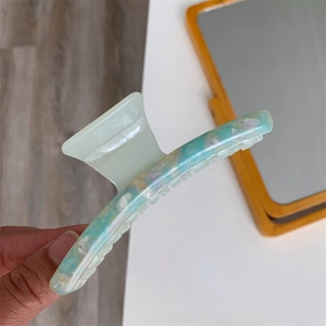 Detail view of a marble texture acetate hair claw clip with blue and green pearlescent finish