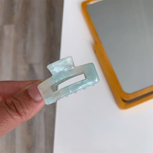 Close-up of mint green acetate hair claw clip with marble texture and rectangular hollow design