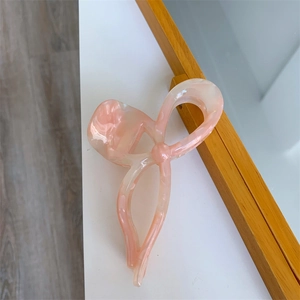 Close-up of pink marbled acetate hair claw clip with a hollow bow knot design on white desk