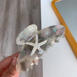 Detail of grey acetate shark clip with three glittery starfish on natural wood background