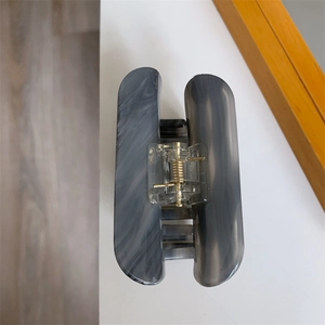Detail view of acetate hair claw clip with grey marble pattern and golden metal spring