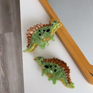 Detailed macro view of two cartoon dinosaur hair claws in green acetate with marble finish