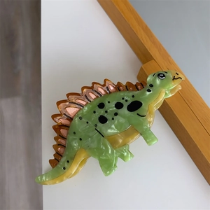 Close-up of a green stegosaurus hair claw clip with orange plates and black spots