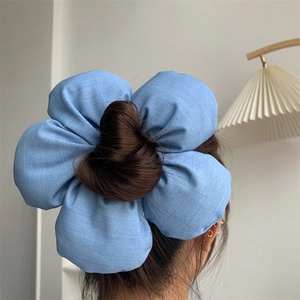 Detail of a large denim blue sponge flower hair scrunchie styled on a bun for women