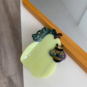 Close-up of creative pear-shaped hair claw with green acetate texture and bee detail
