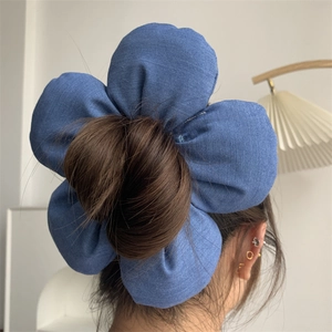 Detail of a large denim blue flower hair tie styling a high bun on a model