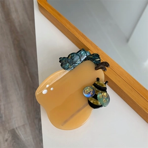 Detail of pear-shaped acetate hair claw clip featuring marble green leaf and bee accent