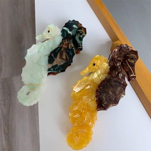 Detail of seahorse-shaped acetate hair claws featuring marble texture and golden accents