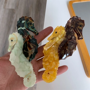 Detailed close-up of acetate seahorse hair claws with marble textures and gold gilded edges
