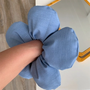 Macro view of oversized denim blue sponge flower hair scrunchie worn on wrist