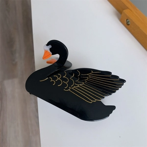Detail of elegant black swan acetate hair claw with golden feather texture and vivid beak