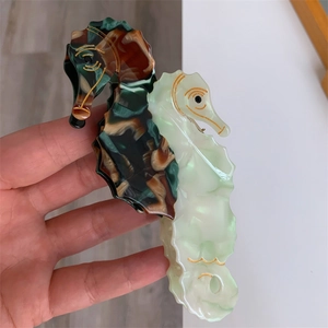 Hand holding sea horse hair claw clip made of tortoiseshell and pearlescent acetate