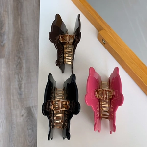 Close-up of three butterfly hair claws in brown, black, and pink with gold metal springs