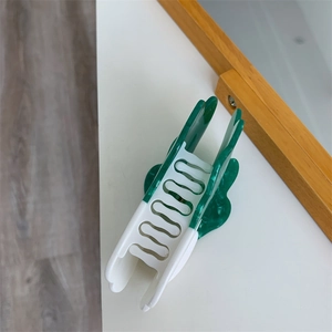 Detail view of flower-shaped hair claw clip in dark green and cream white colors