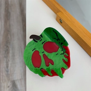 Détail d'une pince à cheveux pomme empoisonnée en acrylique vert avec motif tête de mort rouge