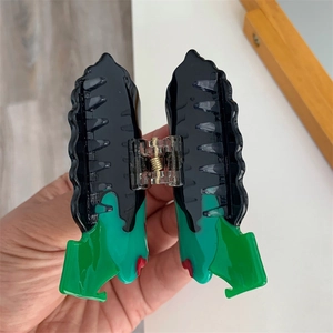 Gros plan d'une pince à cheveux en acétate en zigzag, design ondulé vert, rouge et noir