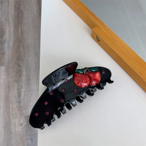 Detail view of a large black hair claw clip with cherry motif and pink rhinestones