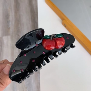 Macro shot of a black hair claw clip with red cherry design and pink rhinestones