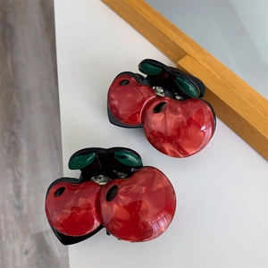 Detailed view of red cherry-shaped hair claws made of marble-textured acetate fiber
