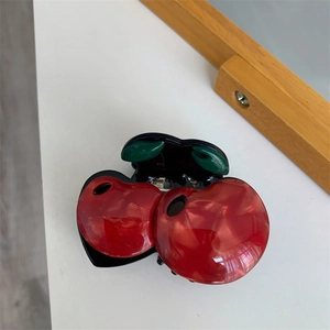 Detail view of a cherry-shaped hair claw with red marble texture and green leaf design