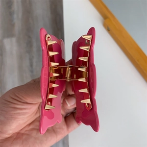 Detail view of pink hair claw clip showing golden metal spring and strong gripping teeth