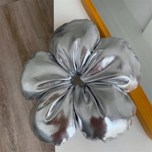 Détail d'un grand chouchou fleur argenté métallique posé sur une surface en bois clair