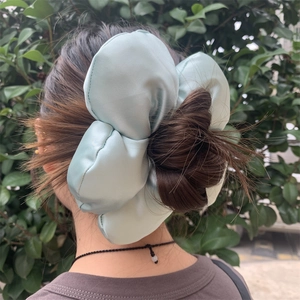 Detail of light mint green satin flower hair scrunchie worn on a brown hair bun