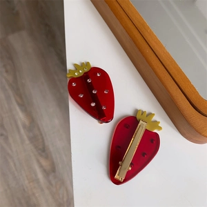 Vue détaillée d'une pince à cheveux fraise en acrylique rouge avec strass et clip doré