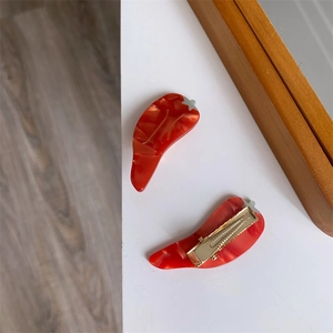 Vue détaillée de pinces à cheveux piment en acétate rouge marbré avec attaches dorées