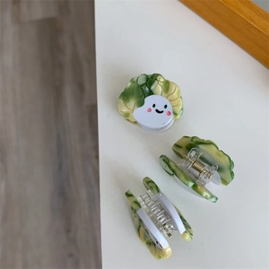 Detalle de pinza creativa con forma de col, cara sonriente y resorte metálico dorado