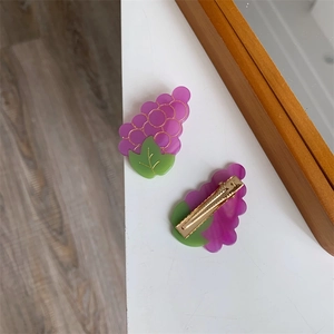 Détail de deux pinces à cheveux en forme de raisin violet en acétate avec attaches dorées