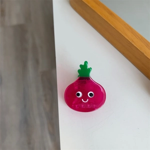 Detalle de una pinza para el pelo rosa con forma de verdura de acetato y cara sonriente