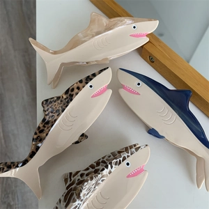 Shark-shaped acetate hair clips in leopard, navy, and grid patterns on a white table