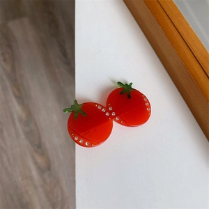 Détail d'une pince à cheveux en forme de tomate rouge avec feuilles vertes et strass