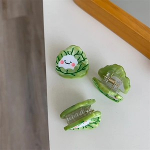 Detalle de pinzas de acetato con forma de col, patrón de hojas verdes y cara sonriente