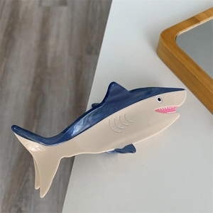Detailed close-up of a blue and white shark-shaped hair claw clip on a wooden desk