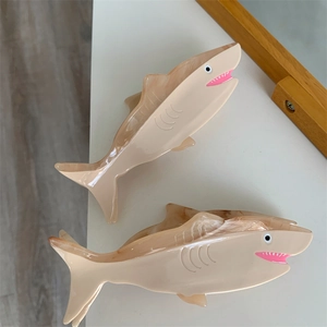 Macro detail of shark-shaped hair claw clips featuring beige marble texture and acetate finish