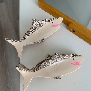 Detail of two cream and tortoiseshell acetate shark hair claws on a white desk