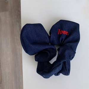 Detail of navy blue denim hair scrunchie featuring red Love embroidery and twill texture