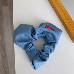Close-up of heart-shaped blue denim scrunchie with red love embroidery on fabric